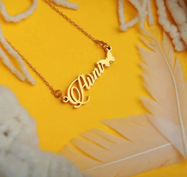 A gold-plated brass alloy pendant with the personalized name 'Hunter' in a cursive script, attached to a chain, displayed on a yellow background with white butterflies and feathers around.
